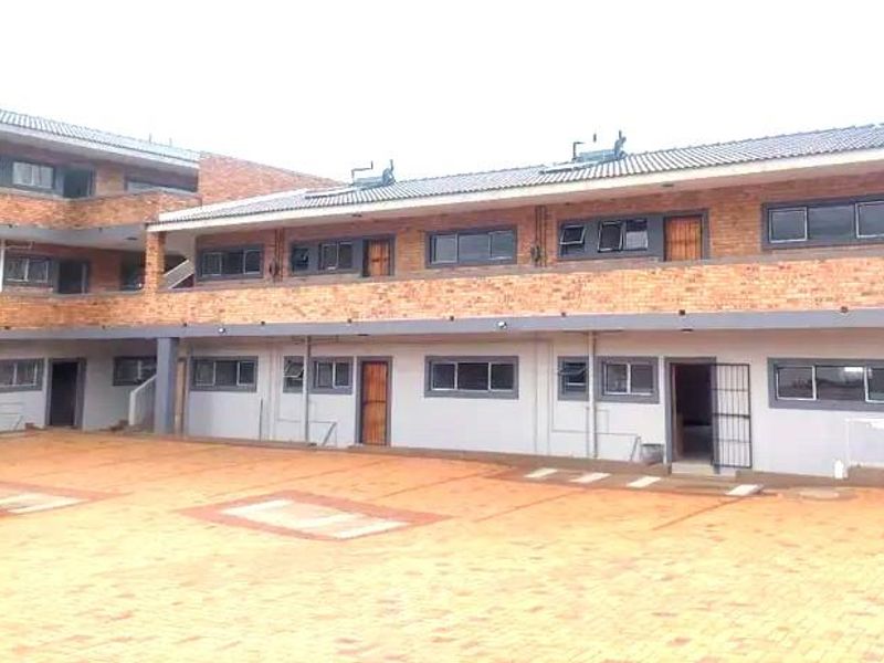 Exterior view of a multi-story apartment complex featuring face brick construction, paved courtyard, and solar geyser installations.