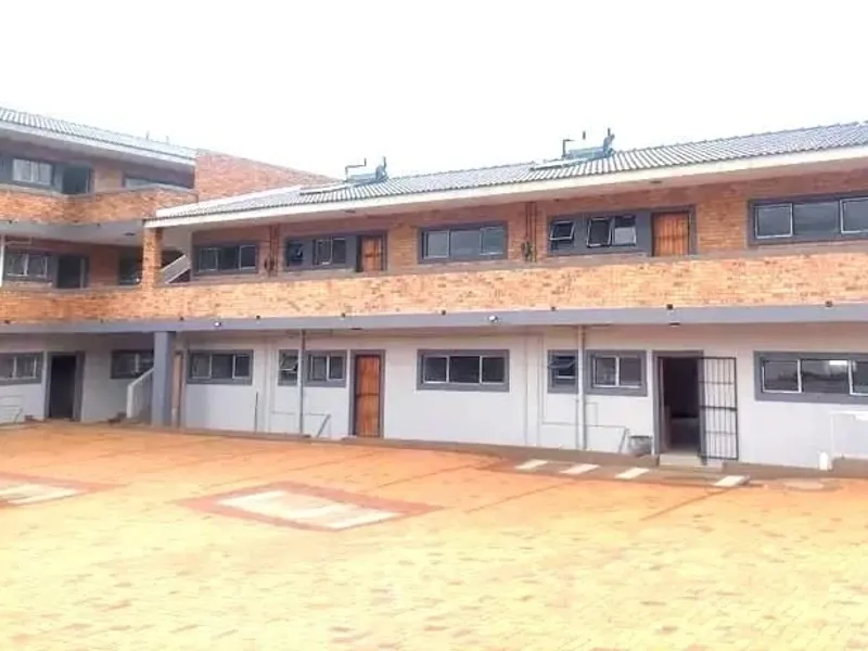 Exterior view of a multi-story apartment complex featuring face brick construction, a paved courtyard, and solar water heating systems on the roof.