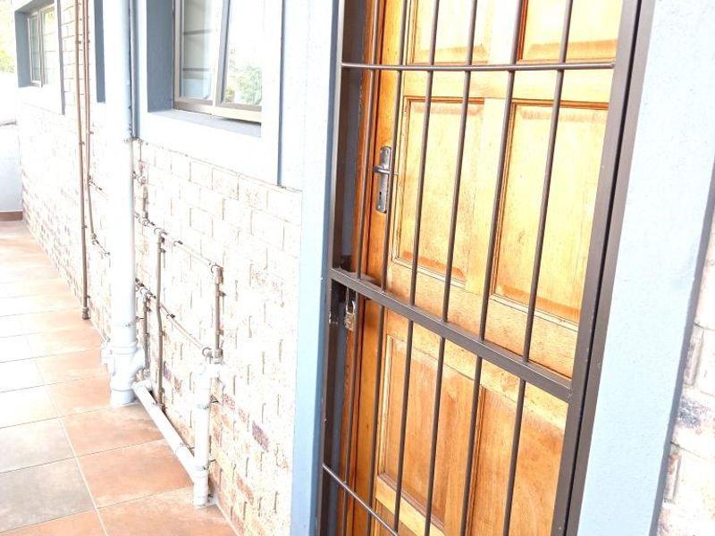 Entrance area featuring a timber door with a security gate, tiled flooring, and exposed external plumbing along the brick facade.