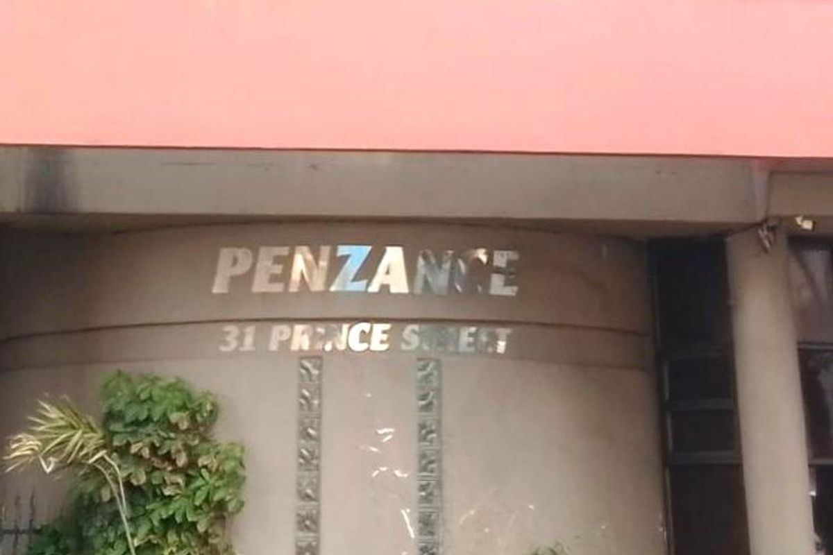 Front entrance facade of Penzance apartment building featuring metallic signage and glass block architectural details.