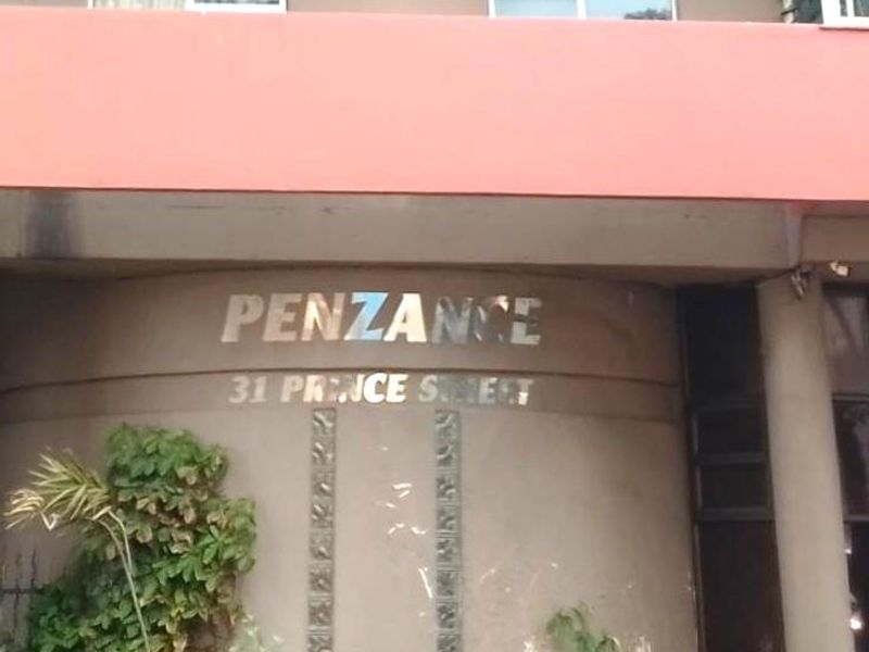 Front entrance facade of Penzance apartment building featuring metallic signage and glass block architectural details.