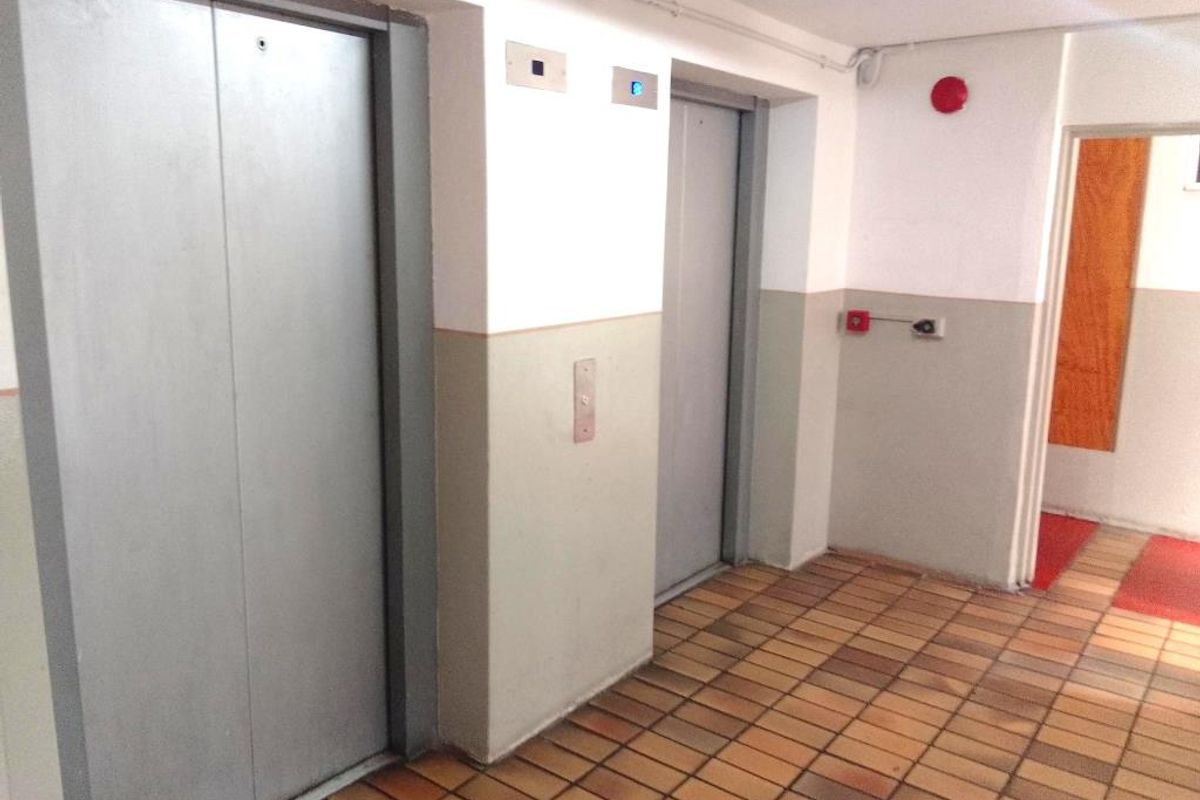 A functional apartment building hallway featuring dual elevators, tiled flooring, and essential fire safety infrastructure.