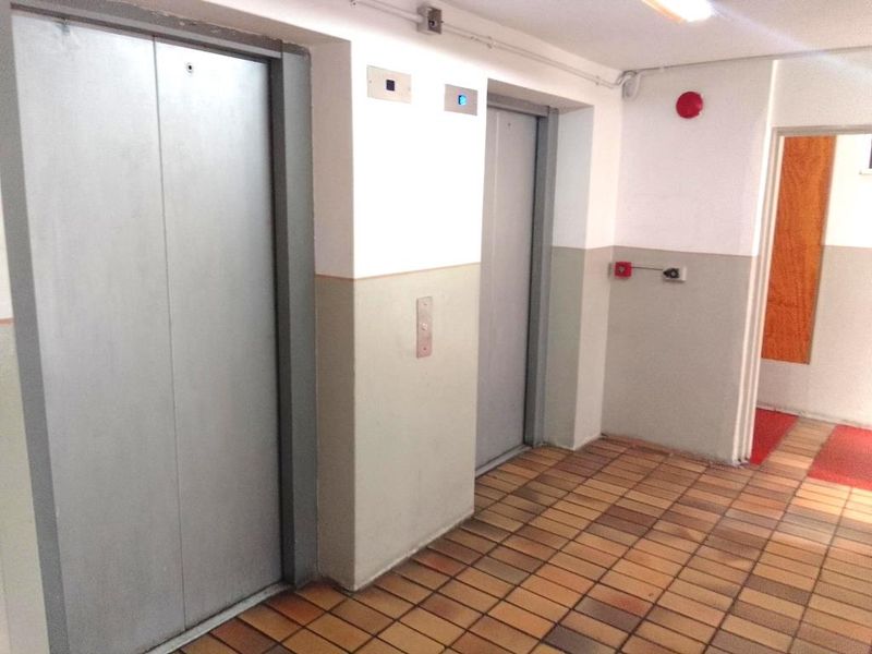 A functional apartment building hallway featuring dual elevators, tiled flooring, and essential fire safety infrastructure.