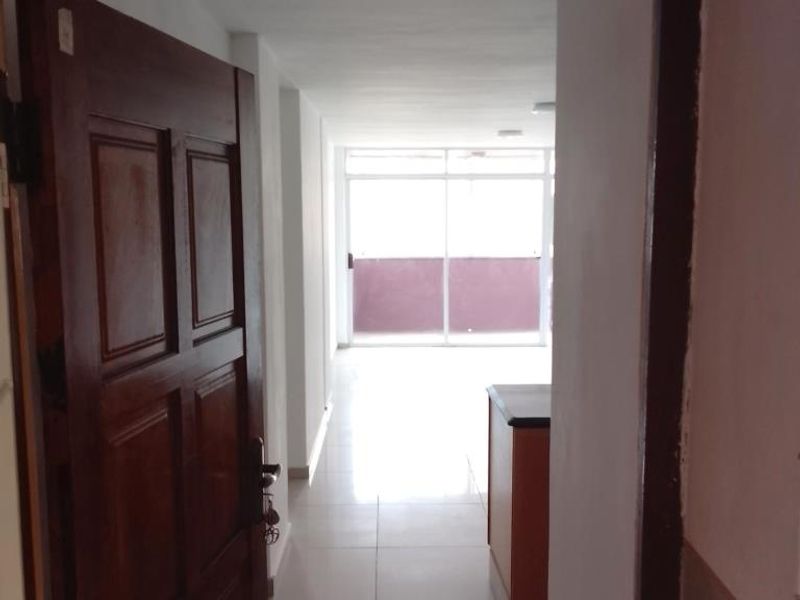 View from the entrance looking into an open-plan living area with tiled flooring and access to a balcony through sliding glass doors.