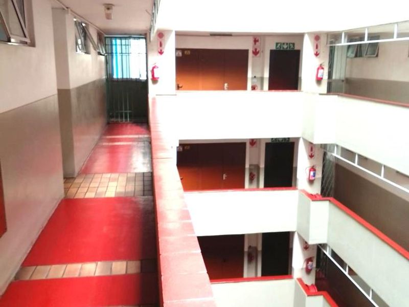 An open-air apartment building hallway featuring a central atrium, tiled flooring, and security gates.