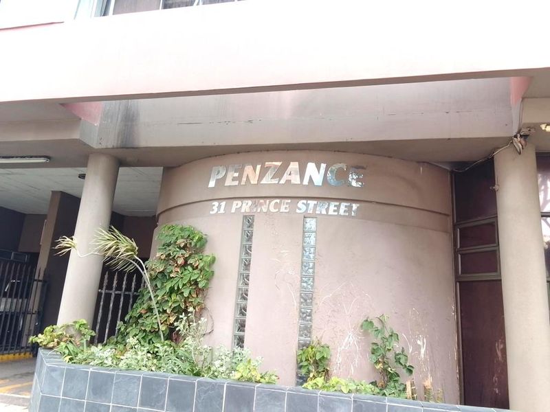 Front entrance facade of Penzance apartment building at 31 Prince Street, featuring concrete structure, glass block accents, and building signage.