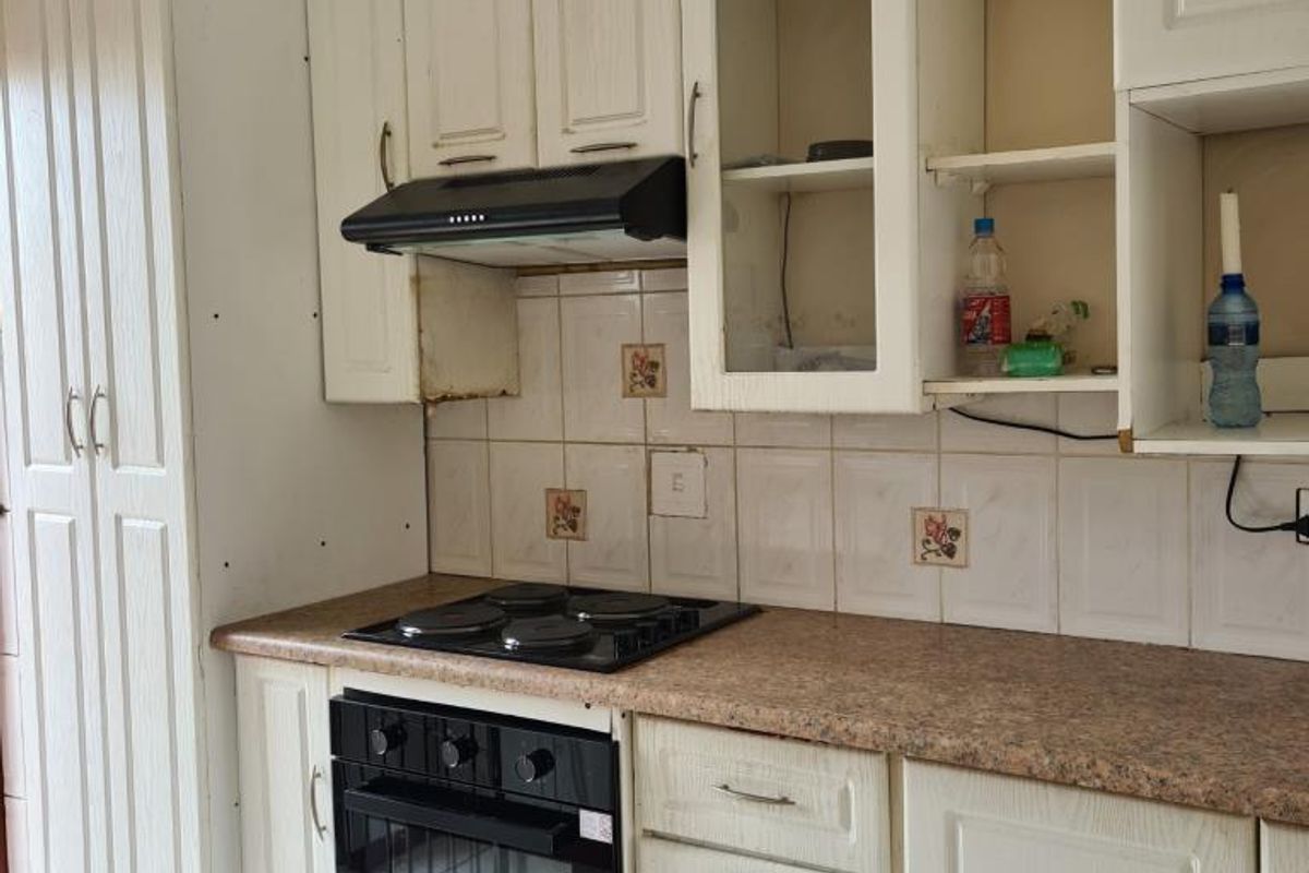 A functional kitchen featuring built-in cabinetry, an electric hob, oven, and extractor fan, with visible wear and tear on the cabinetry and backsplash.