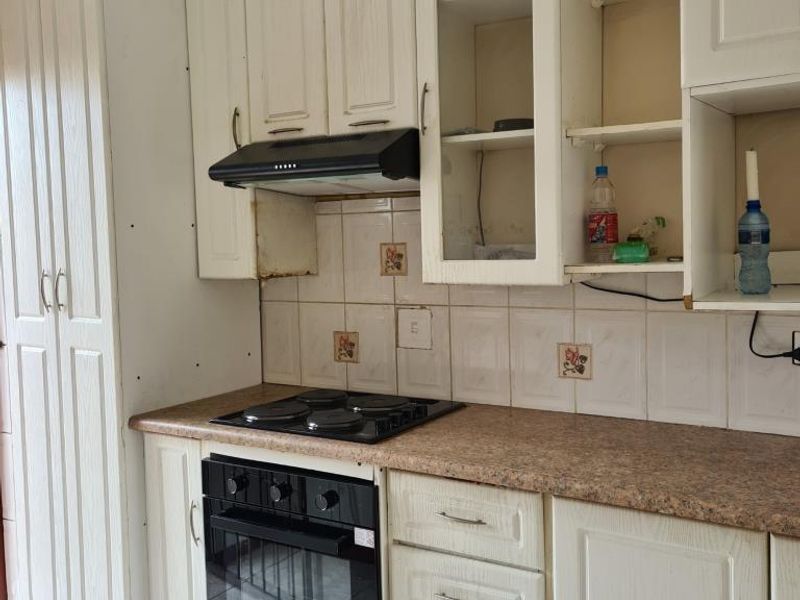 A functional kitchen featuring built-in cabinetry, an electric hob, oven, and extractor fan, with visible wear and tear on the cabinetry and backsplash.