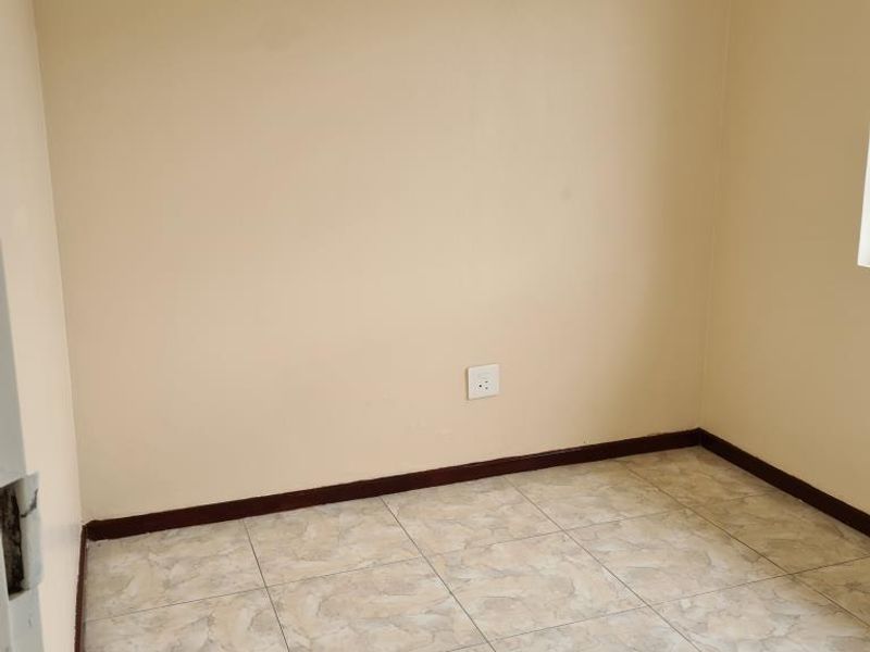 An empty bedroom featuring neutral wall paint, tiled flooring, and a fitted curtain rail, providing a blank canvas for personalization.