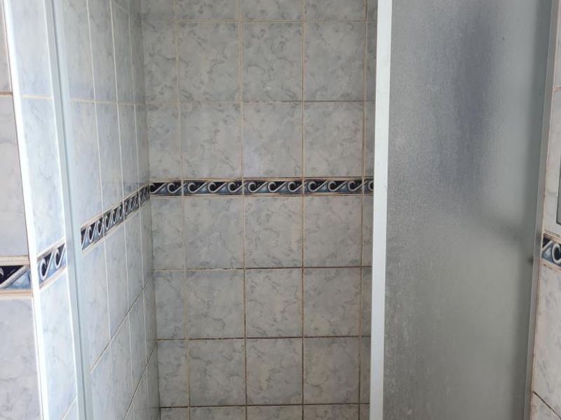A dated shower enclosure featuring patterned wall tiles and a tiled floor, requiring maintenance or renovation to update the bathroom aesthetic.