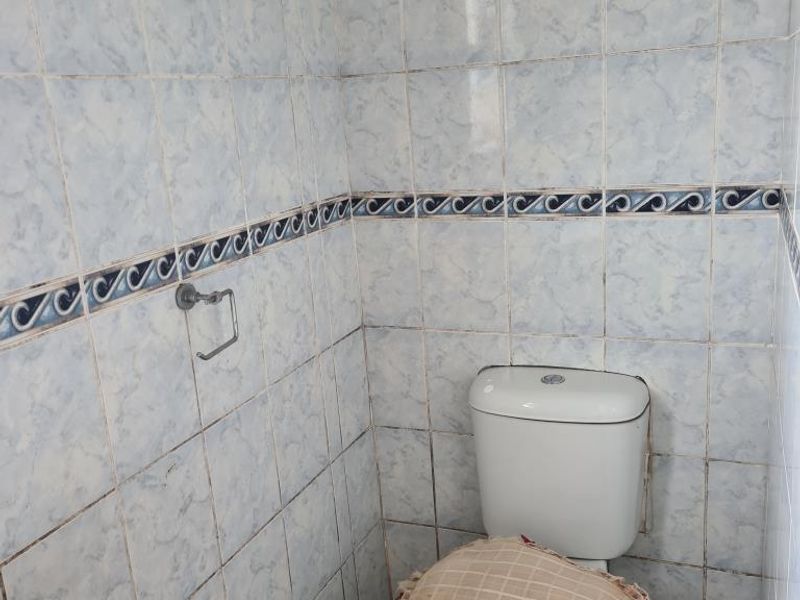 A small bathroom featuring dated ceramic wall tiles, a standard toilet, and a pedestal basin, requiring cosmetic updates to improve its overall condition.