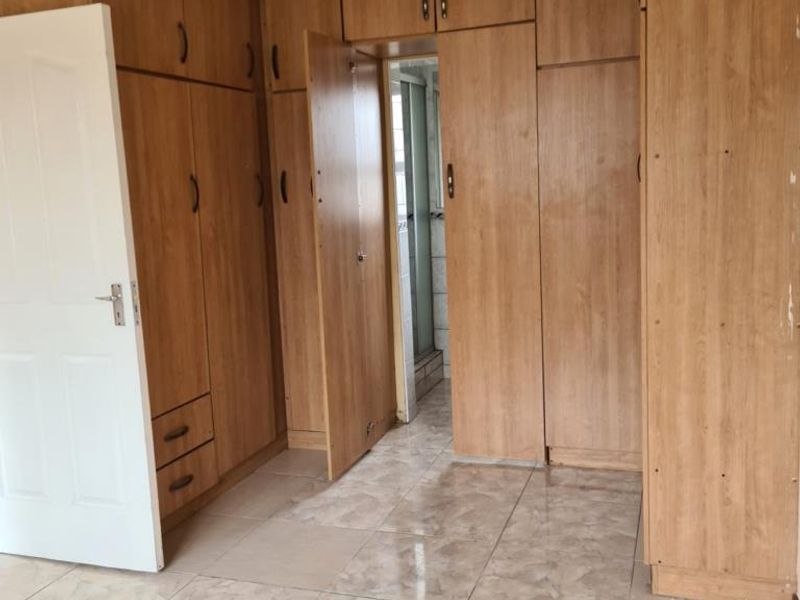 A bedroom featuring extensive built-in wooden cupboards and tiled flooring, offering ample storage space and a neutral foundation for interior design.