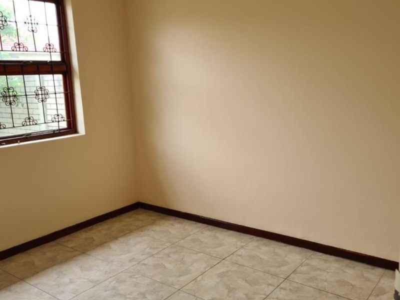 A clean, empty bedroom featuring neutral wall paint, tiled flooring, and a window fitted with security bars.