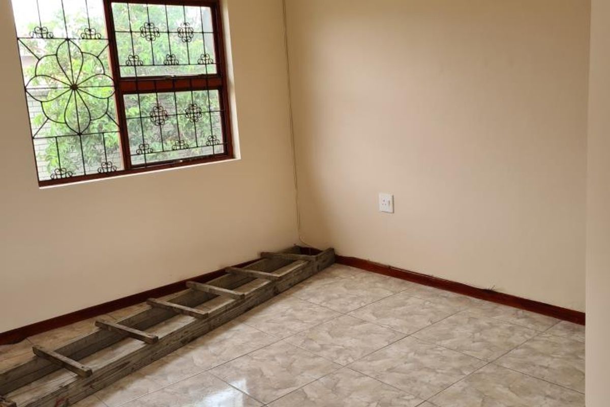 An empty bedroom featuring tiled flooring, neutral walls, and security bars on the window.