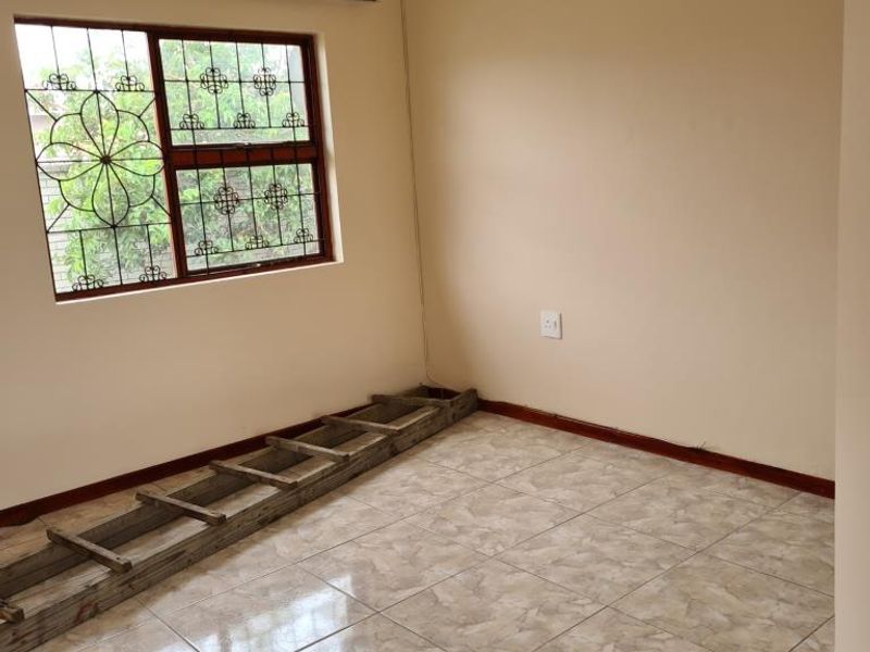 An empty bedroom featuring tiled flooring, neutral walls, and security bars on the window.