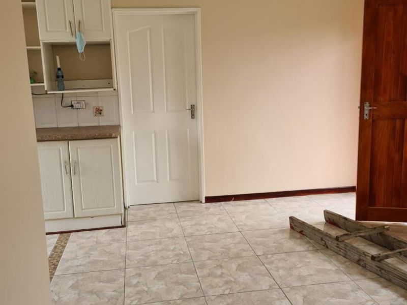 A functional scullery or utility area featuring built-in cabinetry, tiled flooring, and a tiled splashback, currently presented as an empty space.