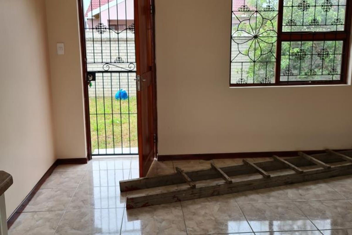 An empty living area featuring neutral wall paint, polished ceramic floor tiles, and secure access via a timber door and window with burglar bars.