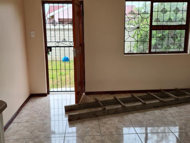 An empty living area featuring neutral wall paint, polished ceramic floor tiles, and secure access via a timber door and window with burglar bars.