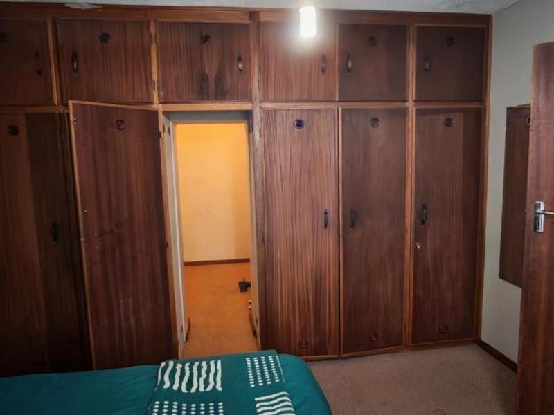 Bedroom featuring extensive floor-to-ceiling built-in wooden cupboards and carpeted flooring, offering ample storage space.