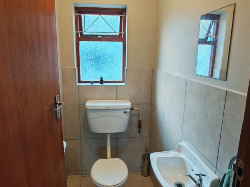 A compact guest bathroom featuring tiled walls, a wall-mounted basin, and a standard toilet.
