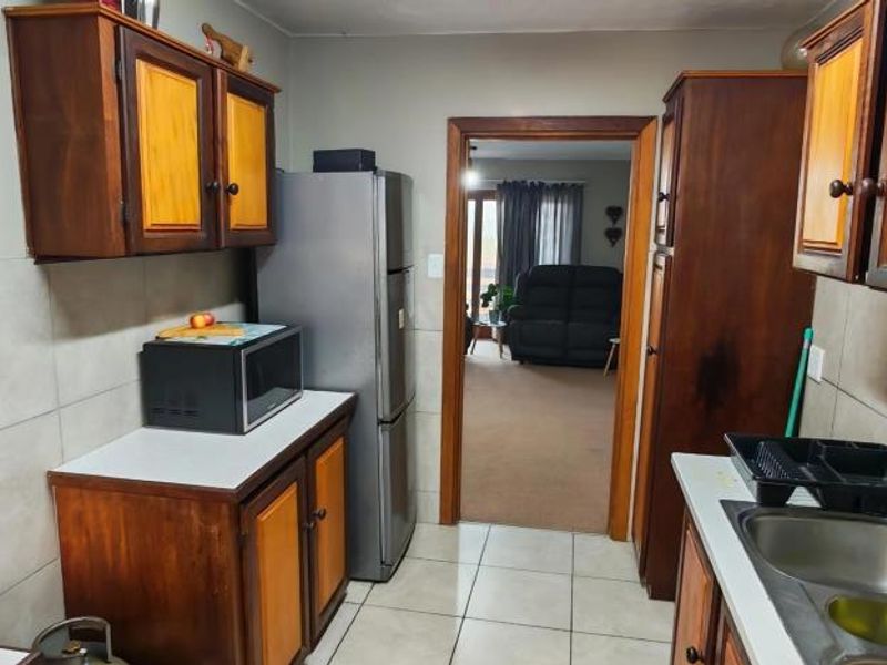 A functional kitchen featuring traditional wooden cabinetry, tiled splashbacks, and a double basin sink, with direct access to the adjacent living area.