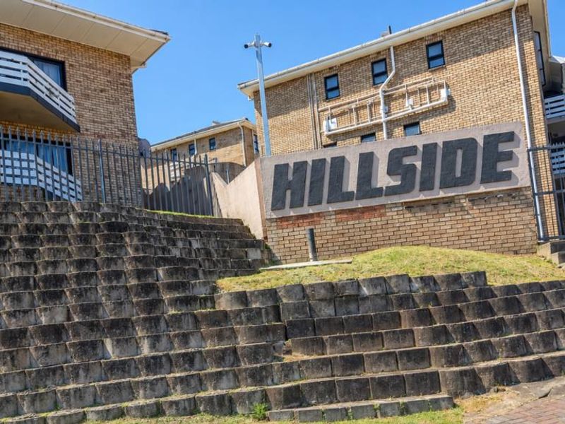 Exterior view of the Hillside townhouse complex featuring brick facade, tiered retaining walls, and security fencing.