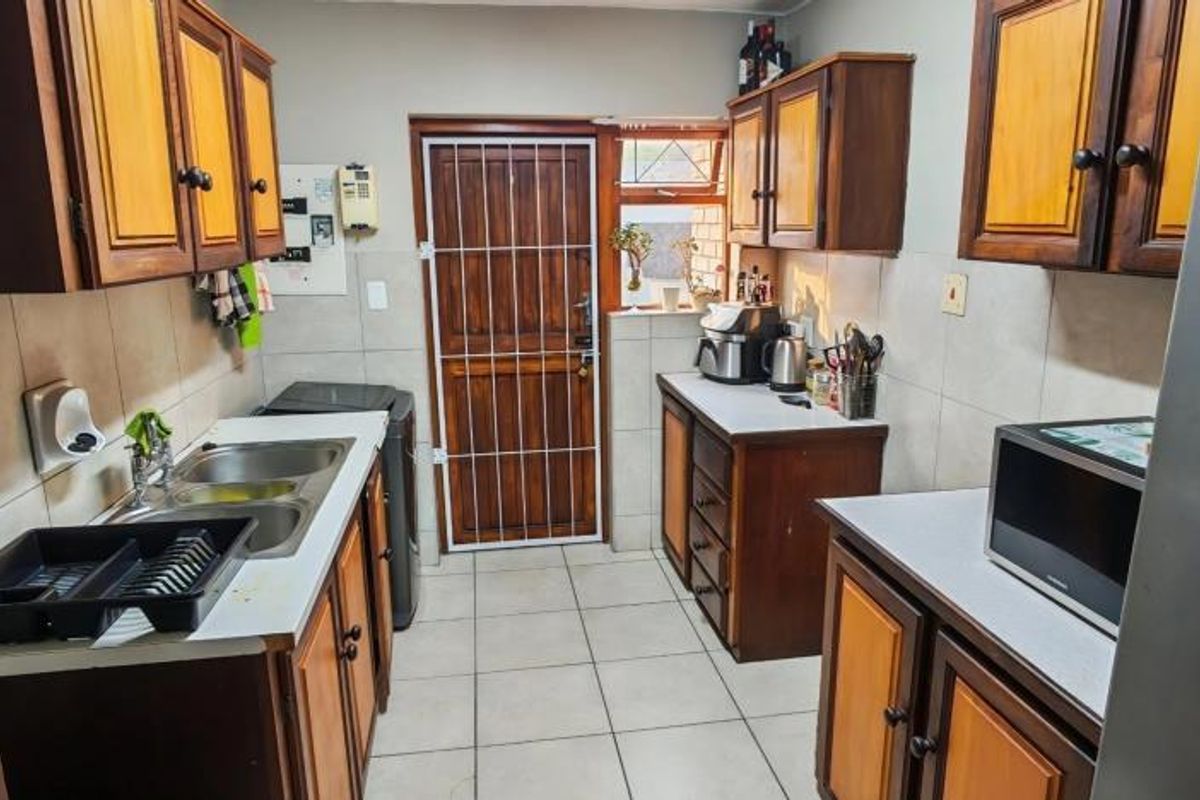 A functional kitchen featuring built-in wooden cabinetry, double basin sink, tiled splashbacks, and direct access to the exterior via a security gate.