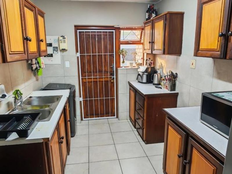 A functional kitchen featuring built-in wooden cabinetry, double basin sink, tiled splashbacks, and direct access to the exterior via a security gate.
