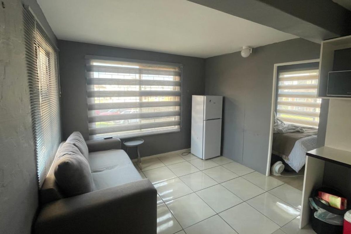 Open plan living area featuring tiled flooring, neutral grey walls, and large windows with fitted roller blinds and security bars.