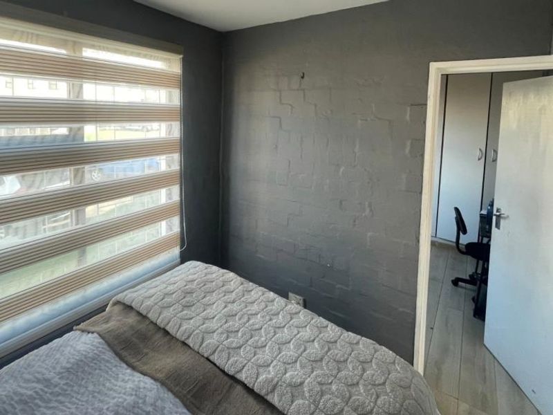 A bedroom featuring an exposed brick wall, modern zebra blinds, and built-in cupboard storage, offering a functional and compact living space.