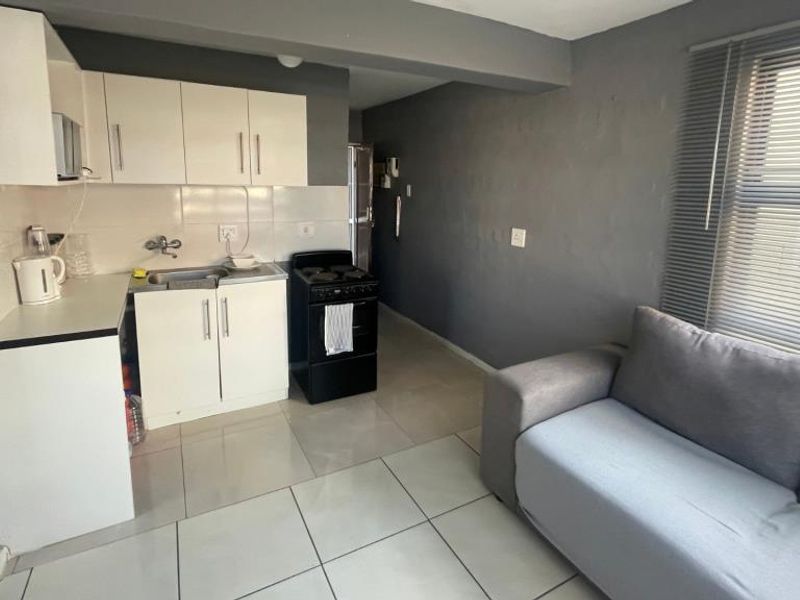 Open-plan living area featuring a compact kitchen with white cabinetry, a freestanding stove, tiled flooring, and neutral grey wall finishes.