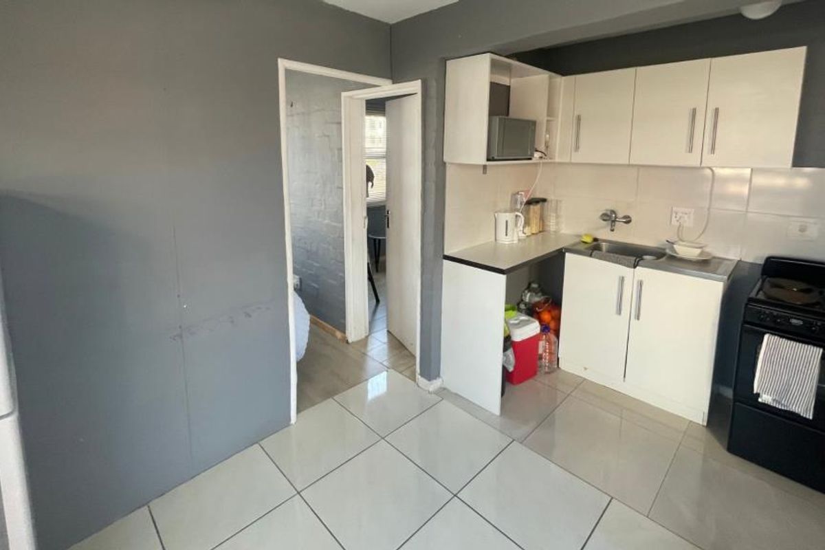 Compact kitchen featuring white built-in cabinetry, tiled flooring, a stainless steel sink, and an electric stove with a tiled backsplash.