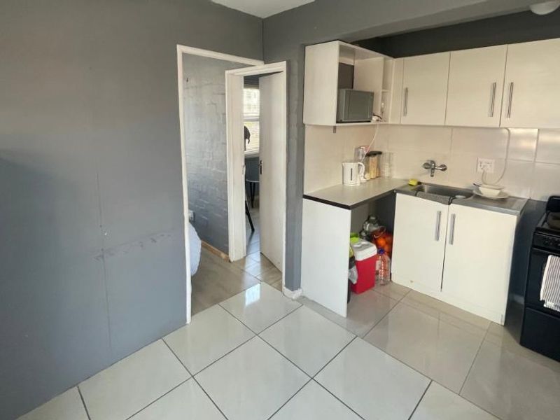 Compact kitchen featuring white built-in cabinetry, tiled flooring, a stainless steel sink, and an electric stove with a tiled backsplash.