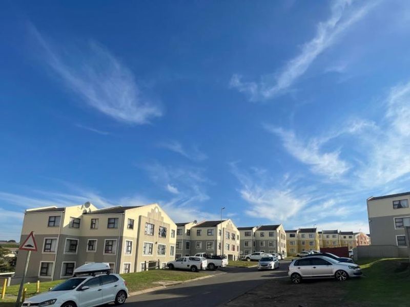Exterior view of a residential apartment complex featuring multiple multi-story buildings, paved access roads, and communal parking areas under a clear blue sky.