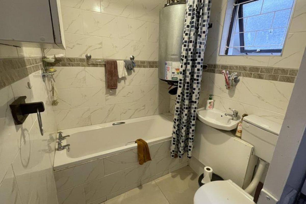A compact bathroom featuring a bathtub, pedestal washbasin, toilet, and a wall-mounted electric water heater with tiled finishes throughout.