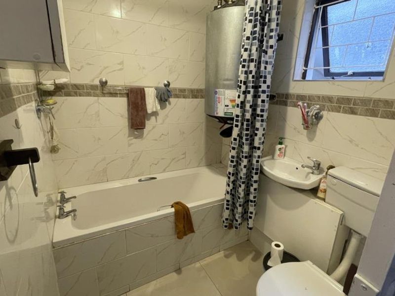 A compact bathroom featuring a bathtub, pedestal washbasin, toilet, and a wall-mounted electric water heater with tiled finishes throughout.