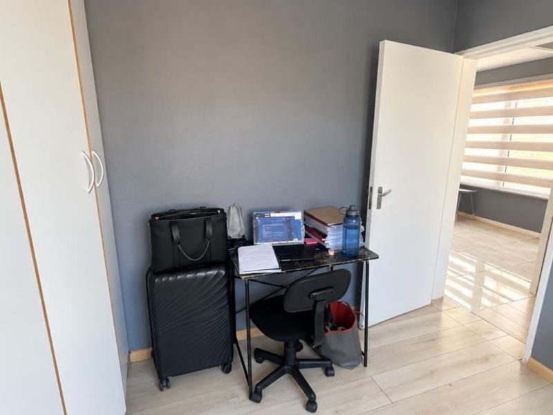 A bedroom featuring laminate flooring and a built-in wardrobe, with a doorway leading to an adjacent room with window blinds.