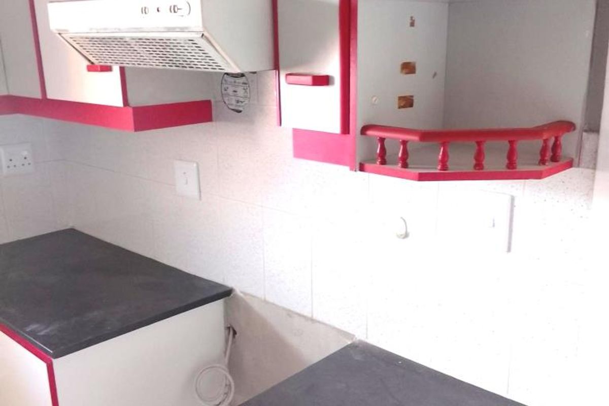 A dated kitchen featuring white and red cabinetry, dark laminate countertops, and a built-in extractor fan, currently vacant and ready for renovation.
