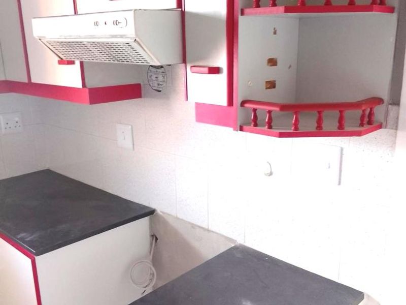 A dated kitchen featuring white and red cabinetry, dark laminate countertops, and a built-in extractor fan, currently vacant and ready for renovation.