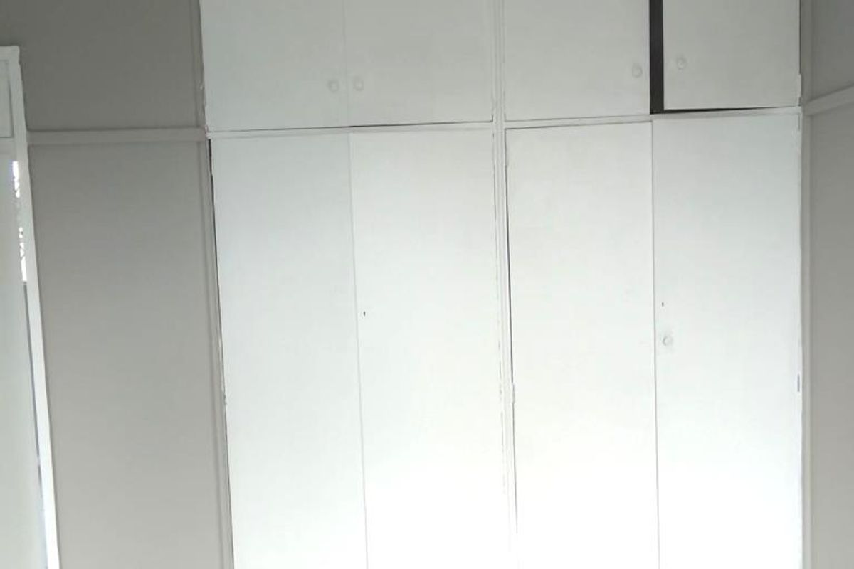 A bedroom featuring built-in cupboards with overhead storage and tiled flooring.