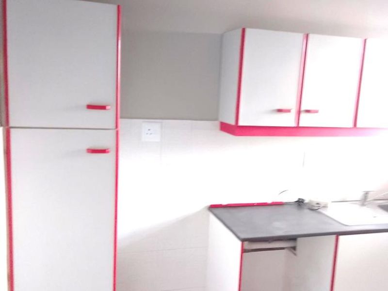 A compact kitchen area featuring white cabinetry with red trim, a tiled backsplash, and a functional sink area.
