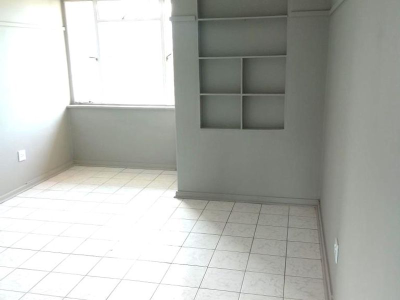 An empty living area featuring neutral grey walls, tiled flooring, and a built-in recessed shelving unit.