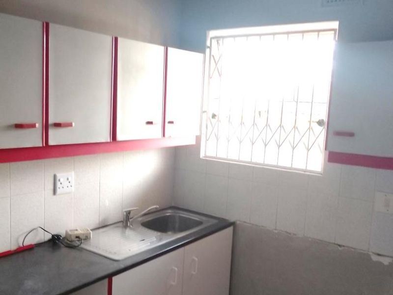 A compact kitchen featuring built-in cabinetry, a stainless steel sink, and tiled splashbacks, requiring some finishing work to the walls.