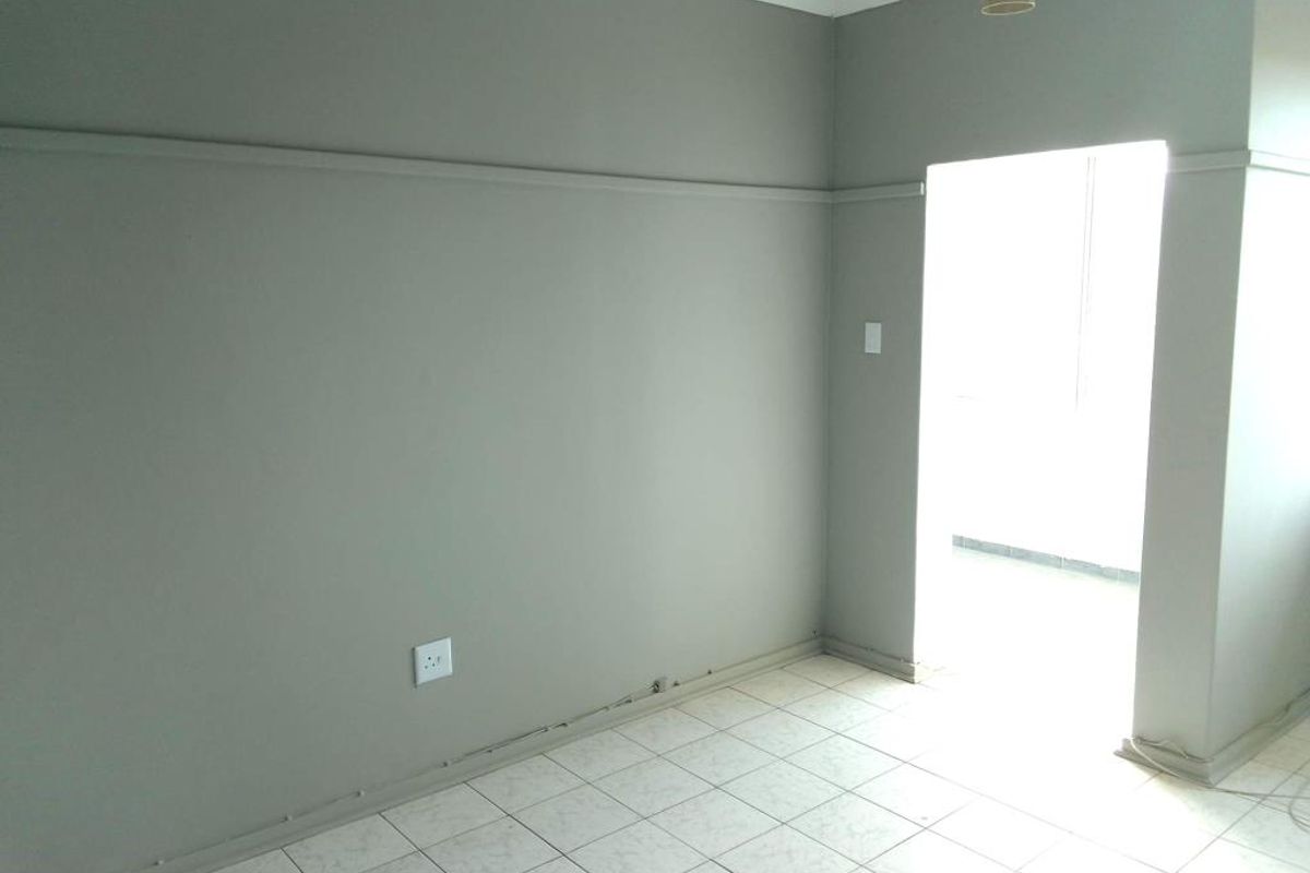 An empty living area featuring neutral grey walls, tiled flooring, and a doorway leading to an adjacent space.