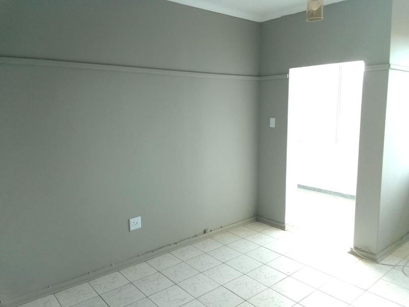 An empty living area featuring neutral grey walls, tiled flooring, and a doorway leading to an adjacent space.