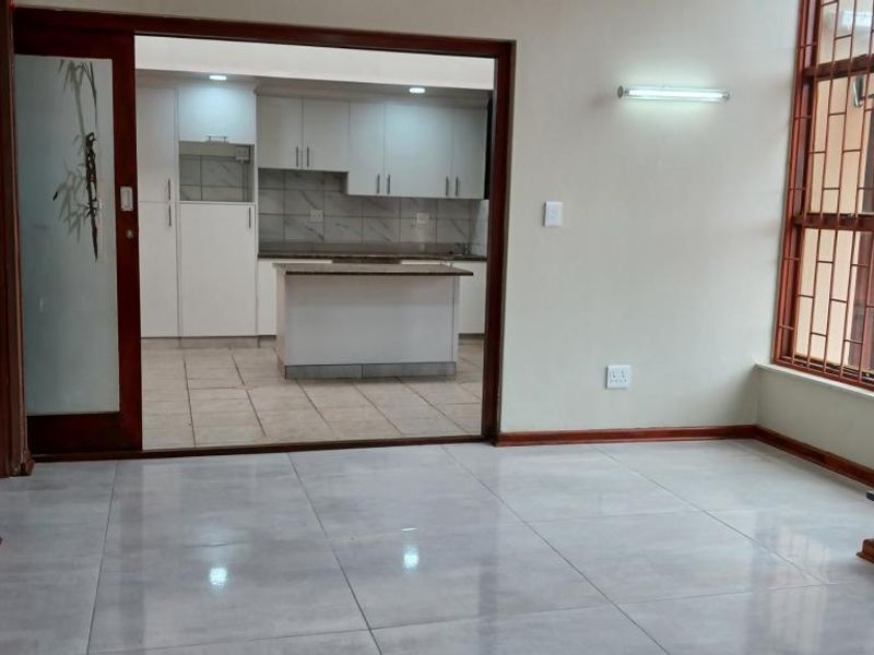 An open-plan living area featuring large format floor tiles, leading into a modern kitchen with white cabinetry and a central island.
