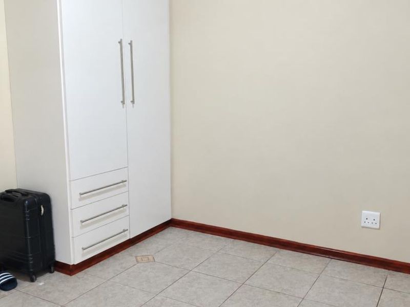 A clean, empty bedroom featuring neutral walls, tiled flooring, and a modern white built-in wardrobe with integrated drawers.