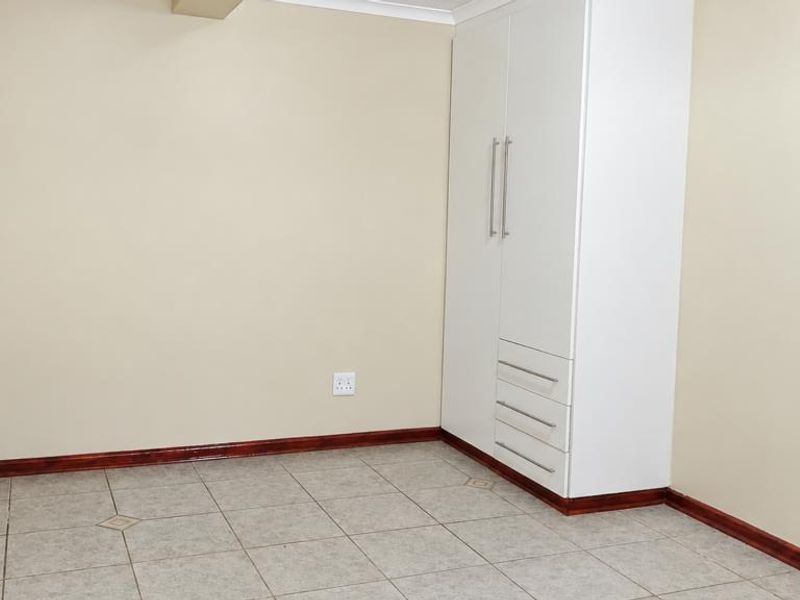 A clean, empty bedroom featuring neutral walls, tiled flooring, and a white built-in wardrobe with integrated drawers.