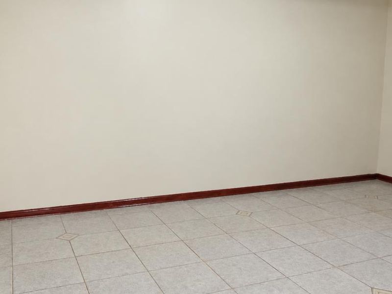 An empty, neutral-toned room featuring tiled flooring and wooden skirting boards, providing a blank canvas for interior design.