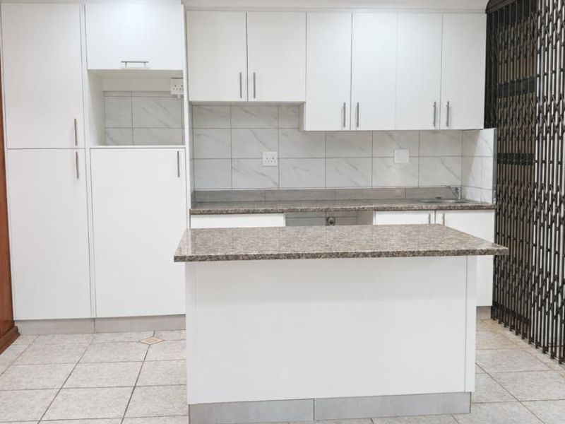 A clean, modern kitchen featuring white cabinetry, granite countertops, a central island, and tiled flooring, providing a functional and bright workspace.